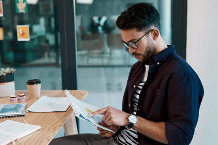 Always going through paperwork. Cropped shot of a handsome young businessman wearing spectacles and sitting alone in his office while reading paperwork.の写真素材