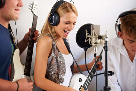 Rocking out. A beautiful young blonde woman singing while her two band members make music in the...