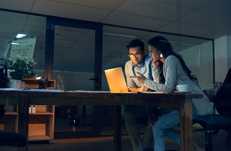 Making important decisions together to improve their chances at success. Cropped shot of two colleagues working late on a laptop in an office.の写真素材