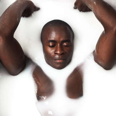 Save some time just for you. Shot of a muscular young man having a milky bath at home.の写真素材