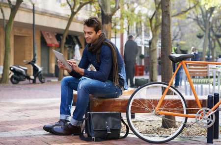 Relaxed city life moments. Shot of a man using his tablet while taking a break in the city with his bicycle beside him.の写真素材