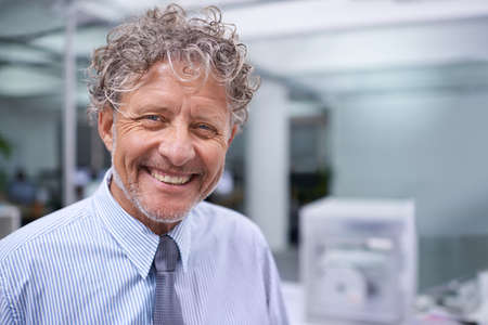 Still facing every workday with a smile. Head and shoulders portrait of a mature businessman in an office.の写真素材