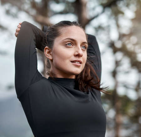 Keeping my end fitness goals in mind. Cropped shot of an attractive young woman stretching before exercising outdoors alone.の写真素材