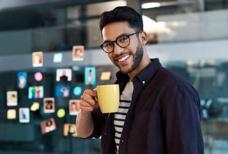 Theres nothing a good cup of coffee cant fix. Cropped portrait of a handsome young businessman wearing spectacles and standing in his office while drinking a cup of coffee.の写真素材