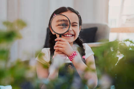 Everything looks bigger. Cropped portrait of an adorable little girl smiling while looking through a...