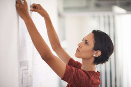 These plans are coming along nicely. Shot of an attractive young architect working in her office.