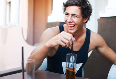 That joke was hilarious. Handsome young guy laughing while enjoying his cold beverage.