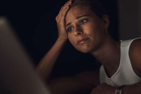 Stress happens when you start working against yourself. Shot of a young businesswoman looking worried while using a laptop during a late night at work.の写真素材