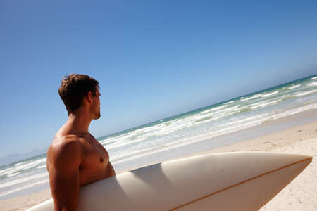 Surfs up. Head and shoulders shot of a young man standing on the beach with his surfboard.の写真素材