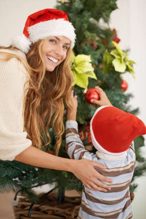 Hes always helping me decorate the tree. Shot of a young boy decorating a christmas tree with his mothers help.の写真素材