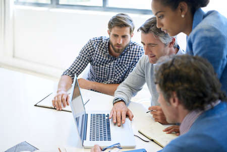 Brainstorming is better with technology. A group of business colleagues discussing work on a laptop during a boardroom meeting.の写真素材