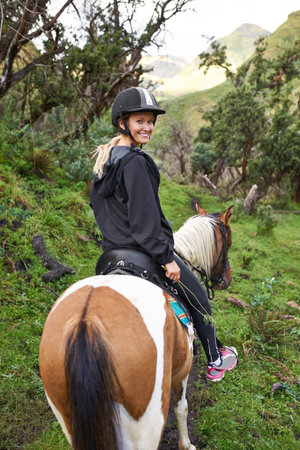 Horse riding in the outback. An attractive young woman riding a horse on a mountain trail.の写真素材