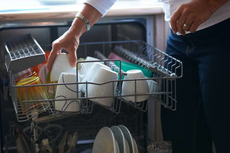 Going about her chores. A senior woman putting her dishes into a dishwasher.