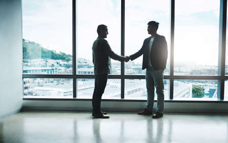 It all comes down to a handshake. Shot of two confident businessmen shaking hands in agreement while standing inside the office during the day.の写真素材