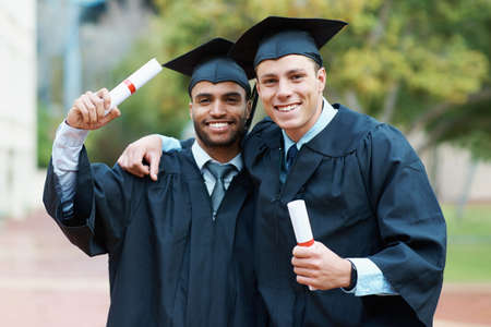 Were on our way to success. Two young college graduates holding their diplomas while wearing cap and gown.の写真素材