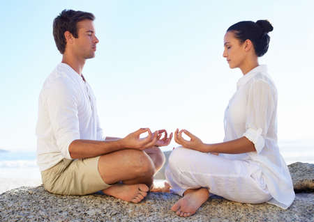 Helping each other peace and tranquility. A young couple performing a relaxing yoga routine together on the beach.の写真素材