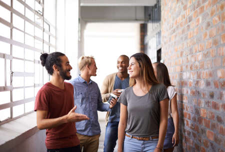 Catching up on the way to class. Shot of a diverse group of university friends talking in a hallway.の写真素材