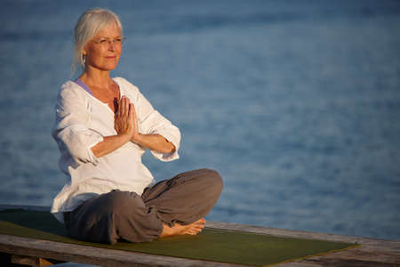 Tranquility by the ocean. Shot of an attractive mature woman doing yoga on a pier out on the ocean.の写真素材