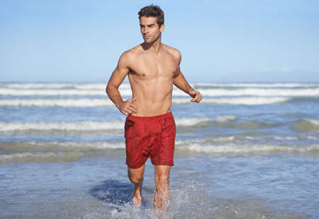 Always alert. A handsome young lifeguard running through the waves.の写真素材