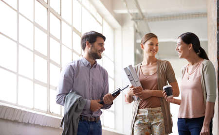 Catching up before a meeting. Shot of a coworkers talking to each other in a office hallway.