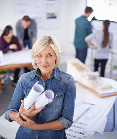 She has big plans for the future. Portrait of a mature female architect standing in an office holding blueprints.の写真素材