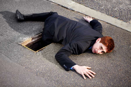 There are many obstacles on the road to success. A young businessman lying on the ground with his leg stuck in a drain.の写真素材