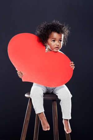 You have my heart. Studio shot of a cute little girl holding a big heart isolated on black.の写真素材