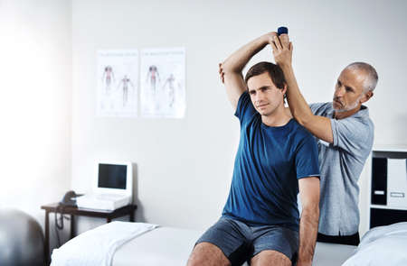 Working on improving his mobility. Shot of a physiotherapist helping a patient work through his...