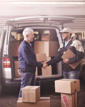 Delivered by the best in the business. Shot of two delivery men shaking hands next to a van filled...