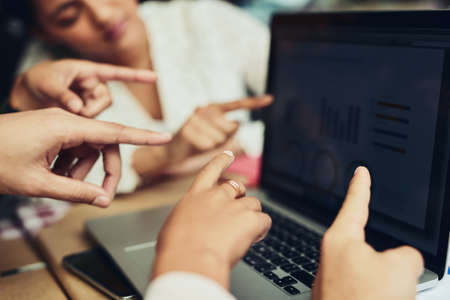 Look at the work together. Cropped shot of unrecognizable designers pointing at information on a laptop screen at a coffee shop.の写真素材