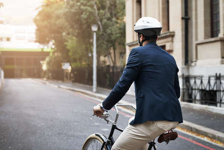 Keep steering forward. Rearview shot of a handsome young businessman riding his bicycle to work in the morning.の写真素材