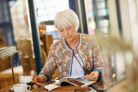Whiling away the day in a cafe. Shot of a senior woman reading a magazine in a cafe.