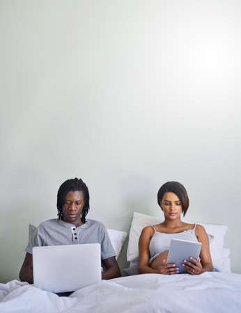 Dont believe everything you read online. Shot of a couple sitting in bed while using wireless...