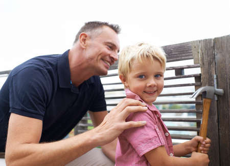 Passing down the knowledge of my many skills. A handsome father teaching his son how to use a hammer.の写真素材