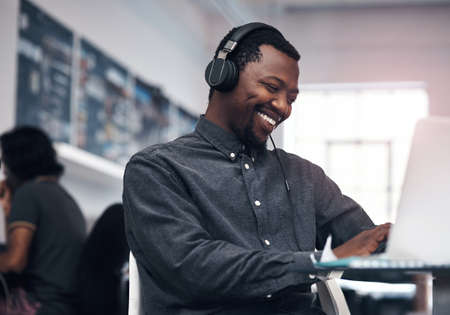 Music makes work so much enjoyable. Cropped shot of a handsome young businessman using a laptop...