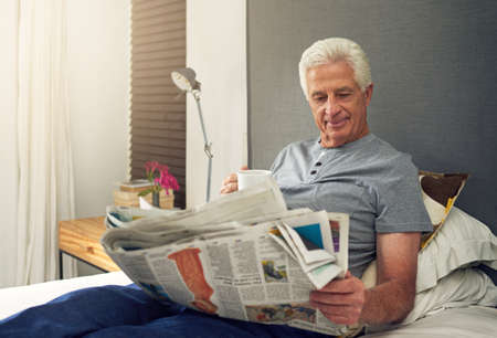 He finds satisfaction in reading good writing. Shot of a senior man reading the newspaper in bed...