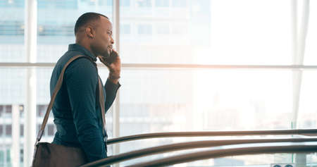 On call and on the move. Cropped shot of a handsome young businessman taking a phonecall while going up an escalator in a modern workplace.の写真素材