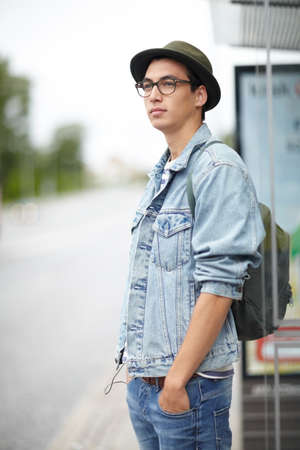 Waiting along the bus route. Hip young guy standing at a bus stop with his hands in his pockets.