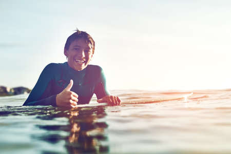 Sun is out, surfs up. Shot of a young boy out surfing.の写真素材