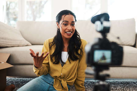 What do you guys think of this. Cropped shot of an attractive young businesswoman sitting in her living room and using her camera to record her vlog.の写真素材