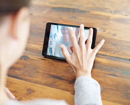 I miss you mom. A young woman using a digital tablet for a video call with her family.の写真素材
