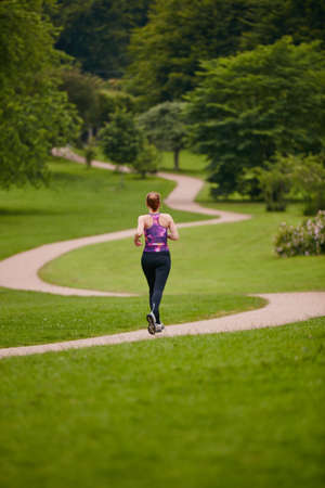 In it for the long run. Rearview shot of a woman jogging along a foothpath in a park.の写真素材