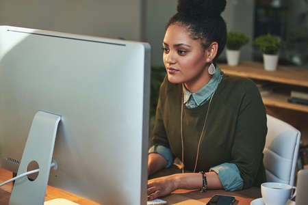 Shes got a deadline to meet. Shot of an attractive young woman working on her computer in the...