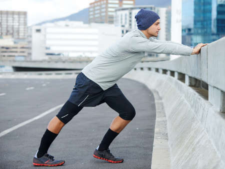 Getting ready for his run. Shot of a young man stretching before a jog through the quiet city...