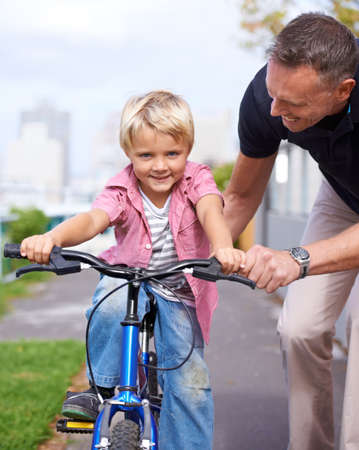 Hes learning fast. A father teaching his young son to ride a bike.の写真素材