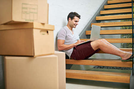Status update Just moved into my new house. Shot of a young man using his laptop while in the...
