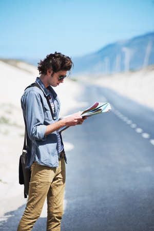 Trying to map out my journey. Young man standing on the side of the road reading a map.の写真素材