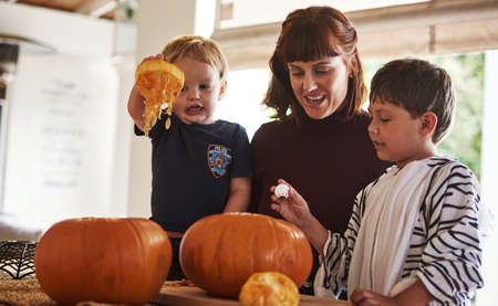 Having the best halloween with my little monsters. Shot of two adorable little boys carving out pumpkins and celebrating halloween with their mother at home.の写真素材