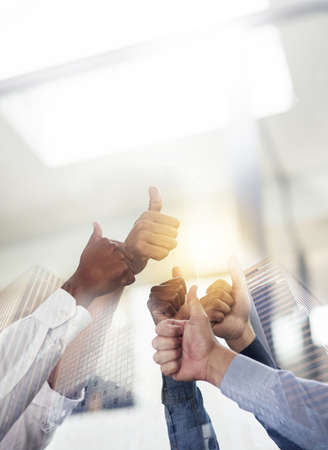 Feeling great about teamwork. Shot of skyscrapers superimposed over an unidentifiable business team giving a thumbs up.の写真素材