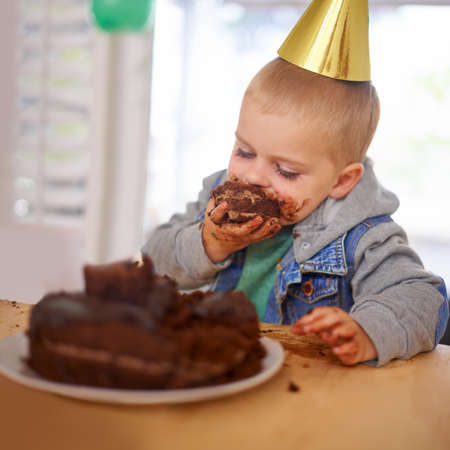 Who left him alone with the cake. Cropped shot of a young boy eating his birthday cake before the party.の写真素材